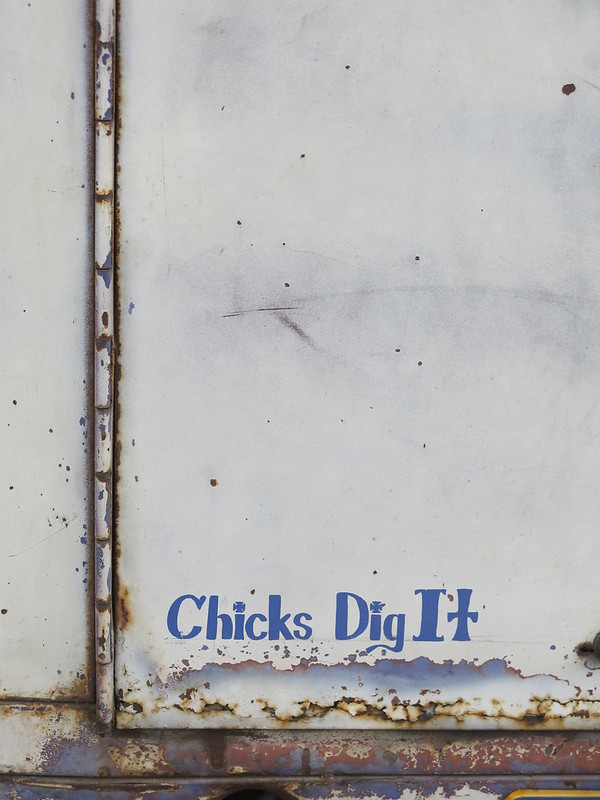An white door on the back of a tractor-trailer rig reads, in blue bubble text, "Chicks Dig It."