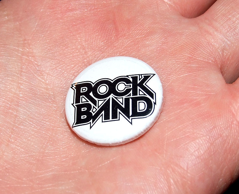 A tiny button printed with the RockBand video game logo rests on someone's palm.